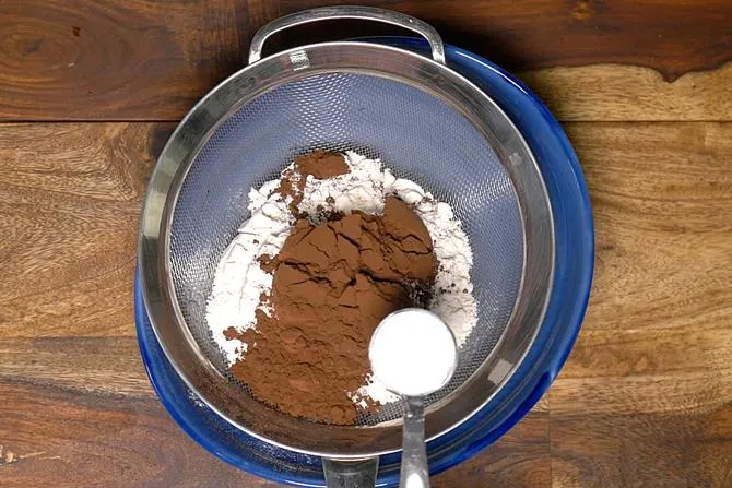 adding dry ingredients to bowl to make eggless chocolate cake