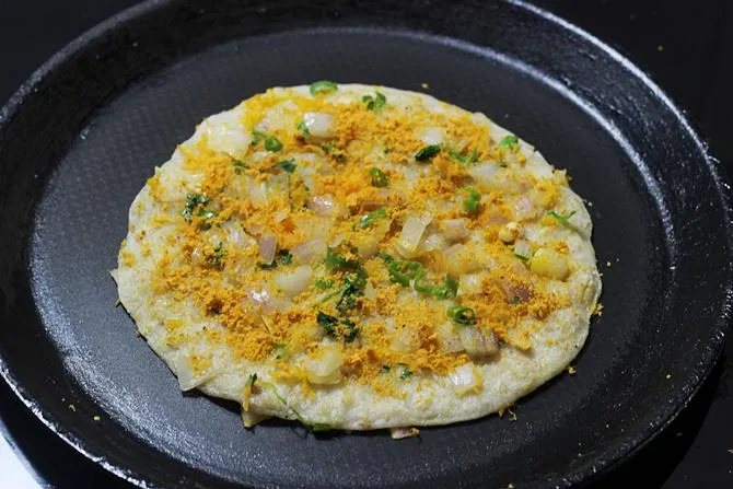 sprinkling spice powders over oats uttapam