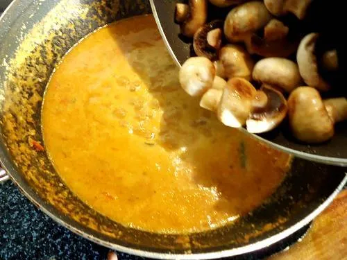 adding mushrooms to simmering curry