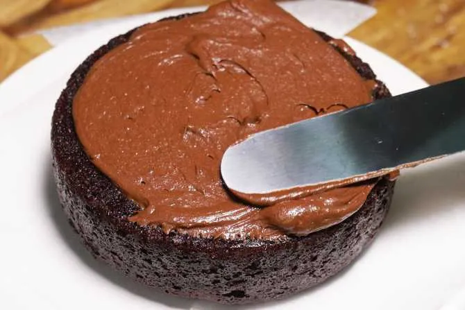 spreading frosting on a chocolate cake  with a spatula