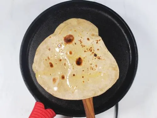 adding ghee to chapati while cooking